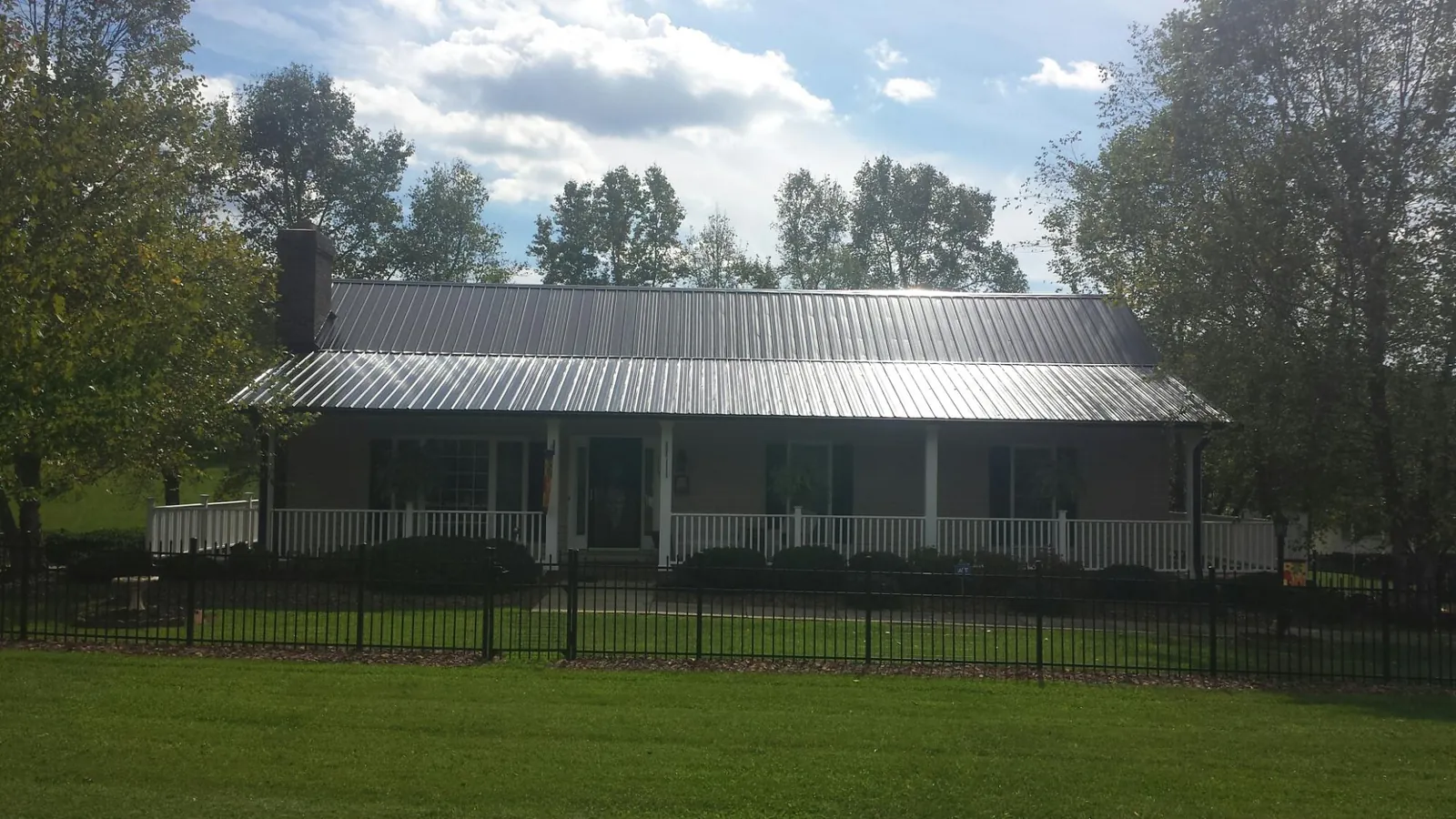 Gray metal roof on a brick ranch with a full width front porch — Gutter Guard Installation work by our crew in Alma